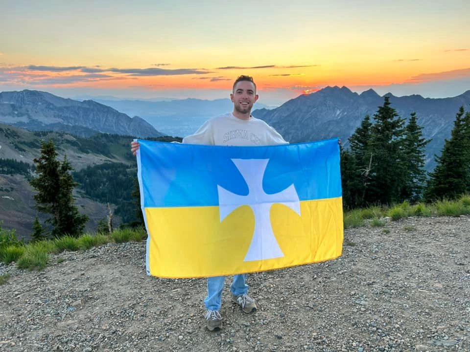 Eta Mu brother holding the White Cross flag in the mountains at sunset