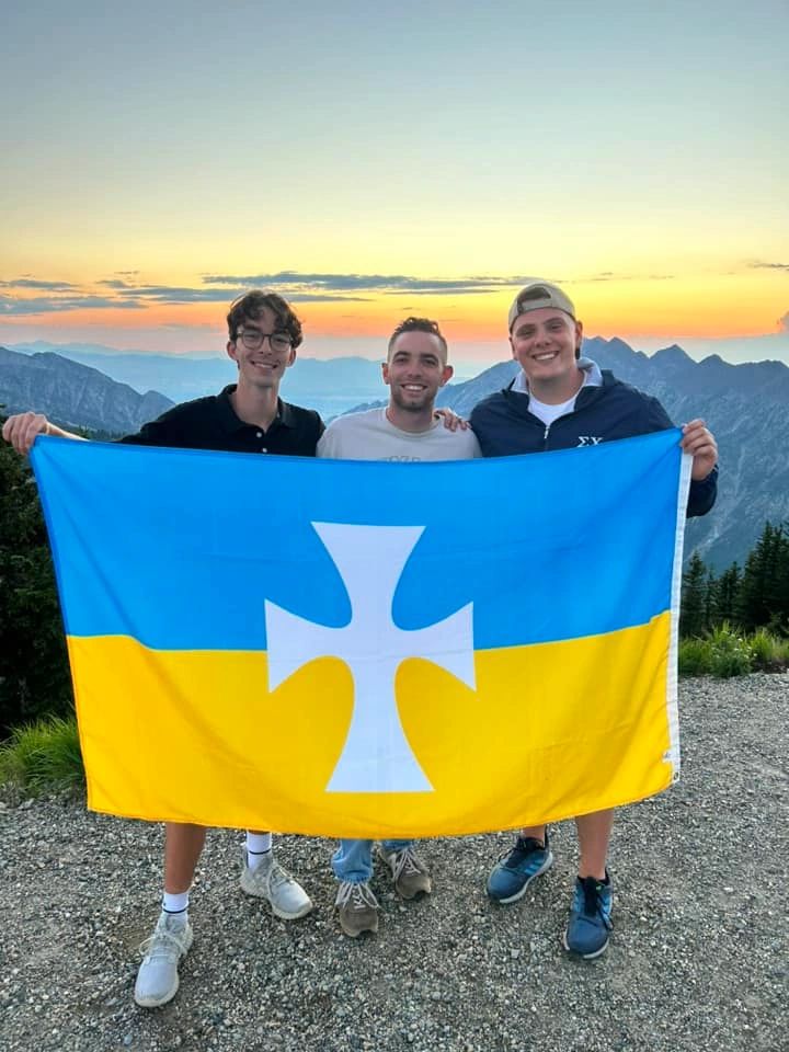 Three Eta Mu brothers holding the White Cross flag in the mountains